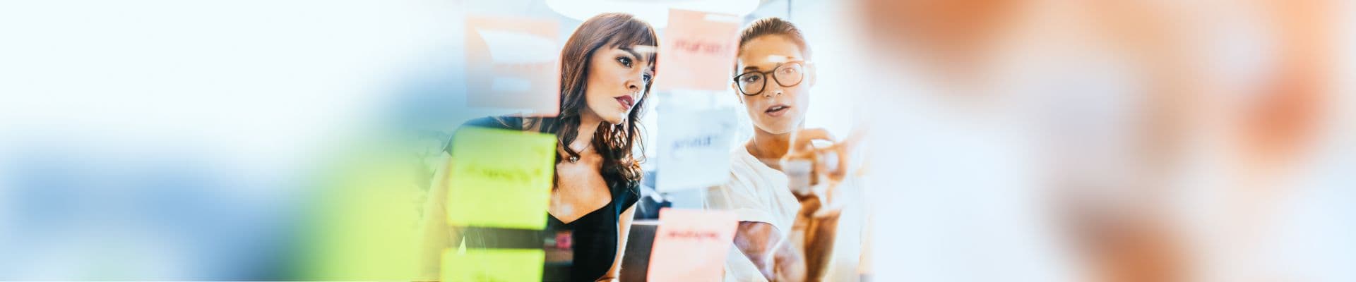 Brainbirds Teilnehmerinnen an einer Glaswand mit Post-its